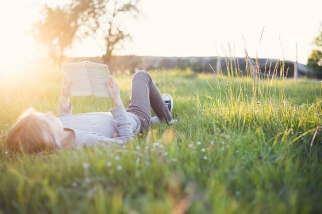 Ferie eller hverdag, kvinne ligger i gresset og leser bok